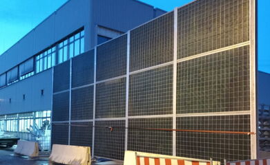 Mobile Lärmschutzwand steht auf dem Asphaltboden und wird von Betonklötzen gehalten