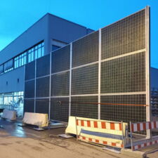 Mobile Lärmschutzwand steht auf dem Asphaltboden und wird von Betonklötzen gehalten