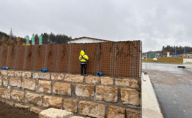 Lärmschutzwand wird auf einer Mauer mit groben Steinen aufgebaut